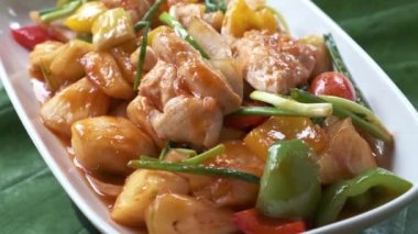 Tatlı ve ekşi tavuk ve sebzeli beyaz tabak kameranın önünde dönüyor.