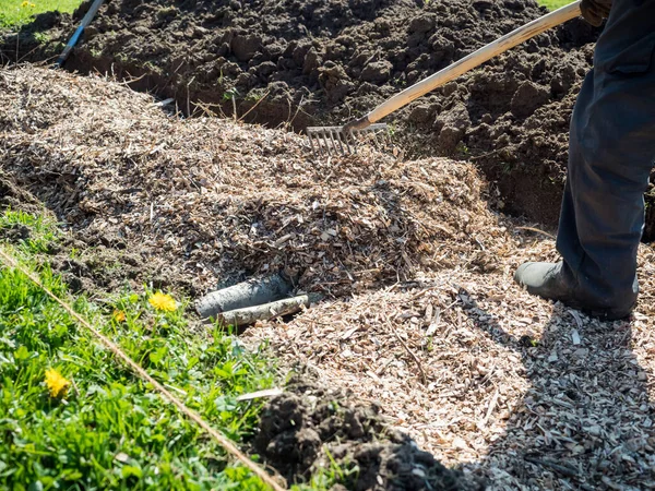 Man spreading shredded wood on top of a permaculture trench with wood logs