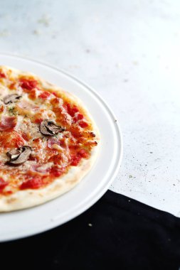 Beyaz tabak ve siyah peçete üzerinde kısmi jambon ve mantarlı pizza manzarası