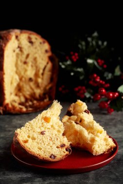 Noel sahnesinde paskalya ekmeği kırmızı tabakta bir parça panettone, arka planda panettone ve ökseotu