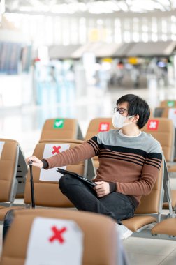 Havaalanı terminalinde yüz maskesi takan Asyalı turist. Coronavirus (COVID-19) yurtdışına seyahat ederken önleme. Sağlık farkındalığı ve sosyal uzaklık kavramı