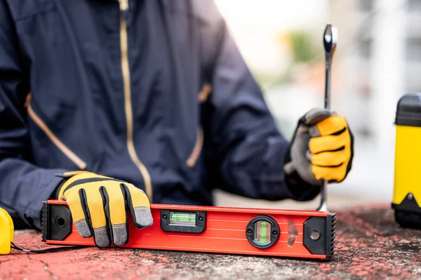 Male mechanic hand or maintenance worker man wearing protective suit holding wrench and aluminium spirit level tool or bubble levels at construction site. Equipment for mechanical engineering project