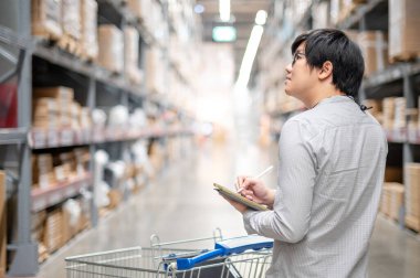 Asyalı işçi, dijital tablet ve kalem kullanarak depodaki raflardaki karton kutularda ürün stokluyor. Fiziksel envanter sayımı konsepti