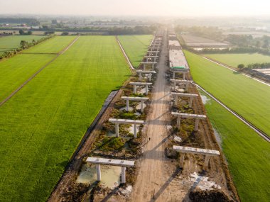 Yeşil pirinç tarlalarından geçen otoyol şantiyesinin havadan görünüşü. Yol Altyapı Projesi. İnşaat mühendisliği kavramı