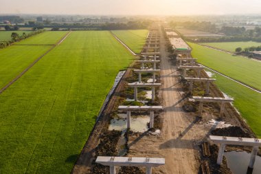 Yeşil pirinç tarlalarından geçen otoyol şantiyesinin havadan görünüşü. Yol Altyapı Projesi. İnşaat mühendisliği kavramı