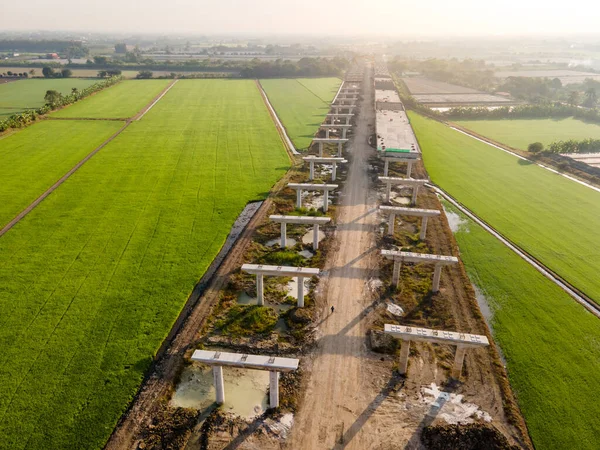 Aerial view of highway construction site passing through green rice fields. Road Infrastructure project. Civil engineering concept