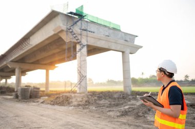 İnşaat alanında proje planlama ve mimari çizimleri için dijital tablet kullanan koruyucu kasklı ve yansıtıcı yelekli akıllı Asyalı işçi ya da erkek inşaat mühendisi..