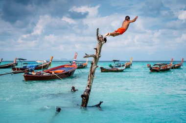 SATUN, THAILAND - 27 HAZİRAN 2020: tanımlanamayan Asyalı çocuk ağaçtan denize atlıyor.