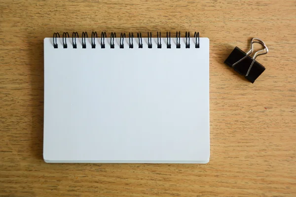 Cuaderno y clip de papel negro en panel de madera —  Fotos de Stock