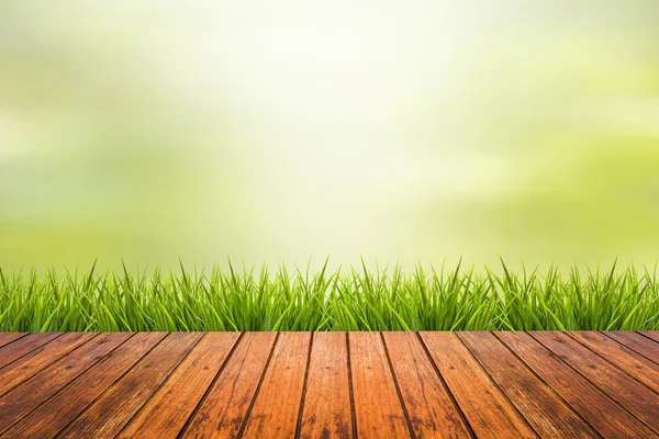 Трава с зеленым размытым фоном и деревянным полом — стоковое фото