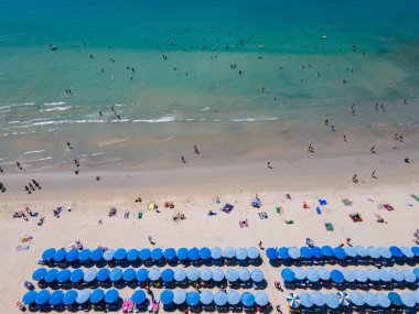 Birçok turistin kumsalda dinlendiği ve Tayland 'ın Phuket kentindeki ünlü bir tatil beldesi olan Kata sahilinde yüzdüğü mavi plaj şemsiyeleri. Andaman Denizi 'nin tropikal kıyılarının havadan görünüşü.