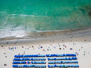 Yaz etkinliği konsepti. Turistlerin kumsalda dinlendiği, havluların üzerinde uzandığı ve Tayland 'ın Phuket kentindeki Kata sahilindeki turkuaz deniz koyunda yüzdüğü mavi plaj şemsiyelerinin hava manzarası..