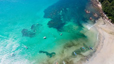 Tayland, Phuket 'te ünlü bir yaz mevsimi olan Kata Sahili' ndeki turkuaz su bölmesinde demirleyen uzun kuyruklu botlarla tropikal kıyı şeridi manzarası..