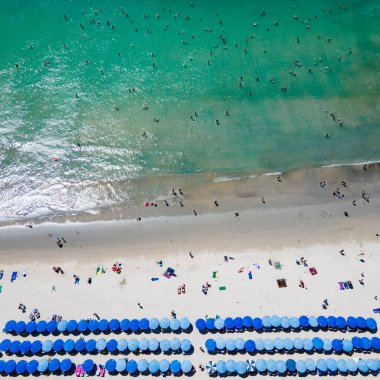 Yaz etkinliği konsepti. Turistlerin kumsalda dinlendiği, havluların üzerinde uzandığı ve Tayland 'ın Phuket kentindeki Kata sahilindeki turkuaz deniz koyunda yüzdüğü mavi plaj şemsiyelerinin hava manzarası..