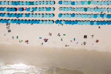 Kumsalda dinlenen turistlerin bulunduğu mavi plaj şemsiyelerinin, Tayland 'ın Phuket kentindeki ünlü bir tatil beldesi olan Kata plajında havluların üzerinde uzandığı hava manzarası. Yaz etkinliği kavramı