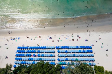 Birçok turistin kumsalda dinlendiği ve Tayland 'ın Phuket kentindeki ünlü bir tatil beldesi olan Kata sahilinde yüzdüğü mavi plaj şemsiyeleri. Andaman Denizi 'nin tropikal kıyılarının havadan görünüşü.