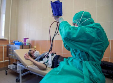 Hijyenik maske ve eldiven takan bir kadın koronavirüs salgınından kaçınmaya çalışıyor. Doktor kan basıncını ölçer..