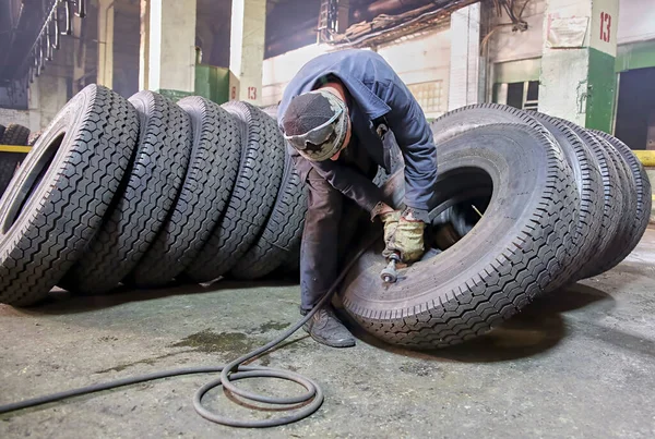 A worker processes a car tire by hand in a tire manufacturing plant.