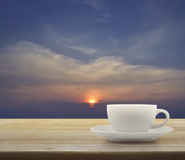 Günbatımı gökyüzü ile ahşap masa üzerinde beyaz Kupası