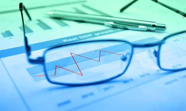 Glasses and pen on blue financial chart and graph, success conce — Stock Photo, Image