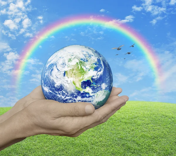 Tierra en manos sobre hierba verde con cielo azul, nube, arco iris y — Foto de Stock