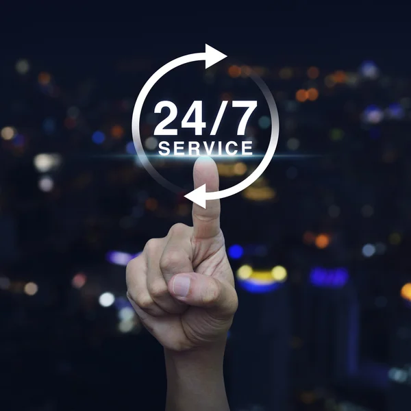 Hand pressing button 24 hours service icon over blurred light ci — Stock Photo, Image