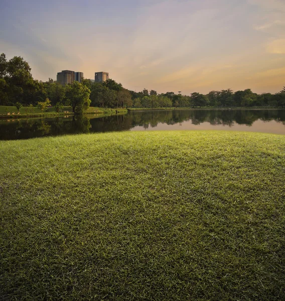Grönt gräs fält med offentlig park över solnedgång himlen — Stockfoto