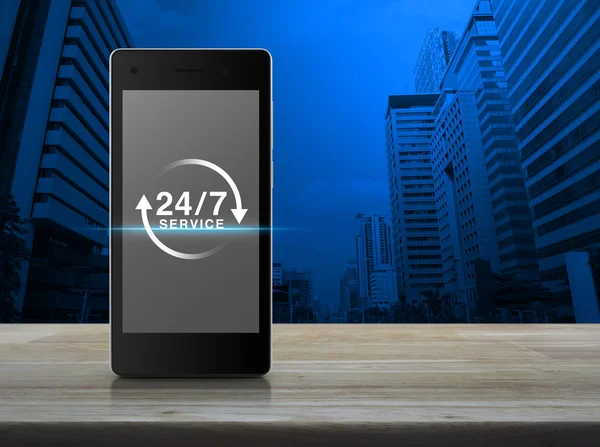 Icono de servicio 24 horas en la pantalla moderna del teléfono inteligente en la pestaña de madera — Foto de Stock