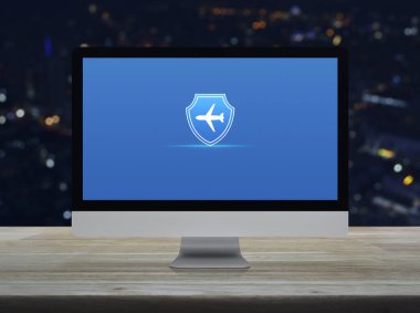 Masaüstünde kalkan düz ikona sahip uçak modern bilgisayar monitörü ekranı ahşap masa üzerinde bulanık renkli gece lambası şehir kulesi ve gökdelen, iş seyahati sigortası ve güvenlik online konsepti