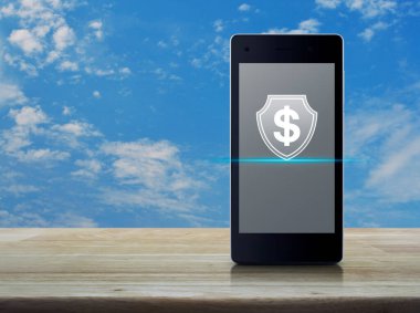 Beyaz bulutlu ahşap gökyüzü, iş parası sigortası ve çevrimiçi korunma kavramı ile ahşap masa üzerinde modern akıllı cep telefonu ekranı üzerinde kalkan yassı simgesi ile dolar