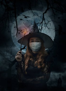 Haç, kilise, karga, kuşlar, ölü ağaç, dolunay ve bulutlu gökyüzü, cadılar bayramı ve koronavirüs ya da covid-19 konsepti üzerinde duran sihirli değnek taşıyan tıbbi maske takan cadılar bayramı cadısı.