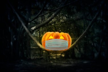 Cadılar Bayramı balkabağı balkabağı mistik ormandaki ağaç gövdesinde tıbbi yüz maskesi takıyor, Cadılar Bayramı ve koronavirüs ya da covid-19 konsepti