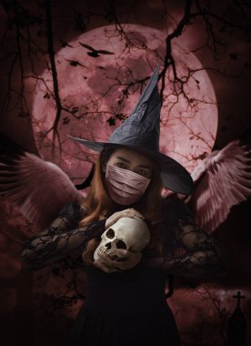Haç, kilise, karga, kuşlar, ölü ağaç, dolunay ve bulutlu gökyüzü, cadılar bayramı ve koronavirüs ya da covid-19 konsepti üzerinde duran bir kafatası tutan tıbbi yüz maskesi takan cadılar bayramı cadısı.