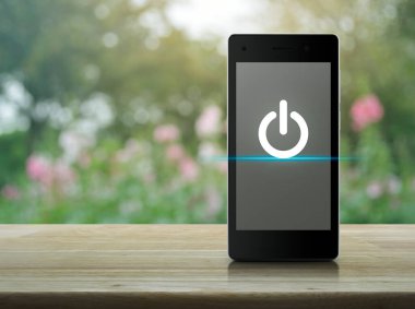 Elektrik düğmesi yassı simgesi, modern akıllı cep telefonu ekranı, ahşap masa, bulanık pembe çiçek ve bahçede ağaç üzerinde, internet üzerinden iş kurma kavramı.