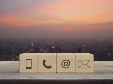 Cep telefonu, telefon, e-posta adresi, blok küplerindeki posta simgesi, ahşap masa üzerindeki şehir manzarası, sıcak gün batımındaki bulanıklık, iş dünyası müşteri hizmetleri ve çevrimiçi destek kavramı.
