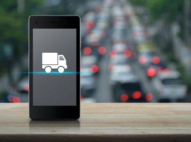 Kamyonet teslimatı düz simgesi, modern akıllı cep telefonu ekranında, ahşap masa üzerinde, trafiğin yoğun olduğu saatte, şehirde arabalar ve yollar, iş ulaşımı online konsept.