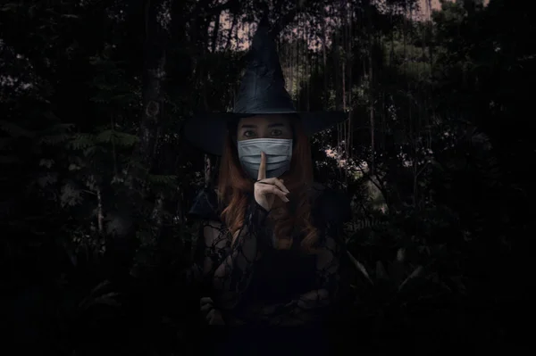 万圣节的巫婆戴着医疗面罩 用手指捂住嘴唇 站在黑暗的森林和树旁 万圣节 头颈蛇或Covid 19的概念上 表示沉默 — 图库照片