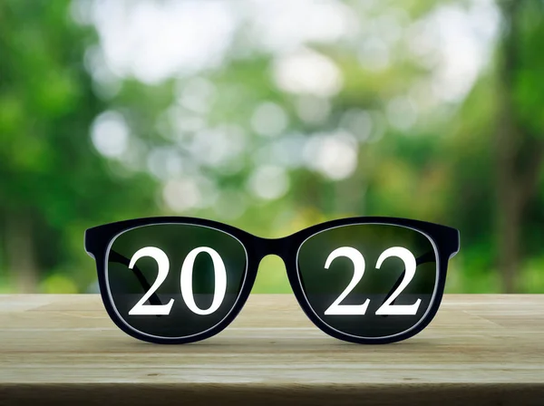 2022 White Text Black Eye Glasses Wooden Table Blur Green — Stock Photo, Image