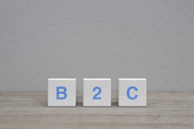 Beyaz blok küpleri üzerine B2C harfi beyaz duvar arkaplanı üzerine ahşap masa, müşteri pazarlama ve strateji konsepti iş