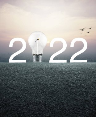 2022 beyaz yazı ve ampul, içinde rüzgar türbini olan yeşil çimen tarlasında günbatımında şehir manzarasının havadan görünüşü, klasik tarzda, mutlu yeni yıl ekolojik kapak kavramı.