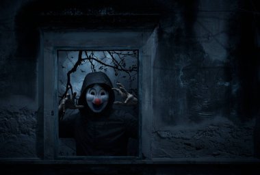 Korkunç kötü palyaço ceketi eski hasarlı pencerede duruyor haçın üzerinde duvar, kilise, kuşlar, ölü ağaç ve ürkütücü bulutlu gökyüzü, Cadılar Bayramı gizemi konsepti