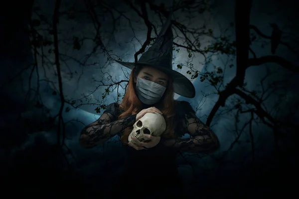 死んだ木 カラス 満月と不気味な曇りの空 ハロウィーンとコロナウイルスまたはCovid 19の概念の上に立って頭蓋骨を保持している医療用フェイスマスクを身に着けているハロウィーンの魔女 — ストック写真