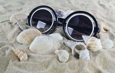 Güneş gözlüğü ve kabukları üzerinde sahil kumu