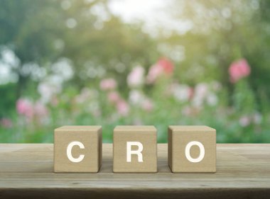 Tahta küpler üzerine CRO kısaltma harfi. Bulanık pembe çiçek ve parktaki ağaç üzerine ahşap masa. Dönüşüm Oranı İyimserleştirme kavramı.