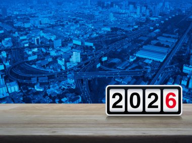Modern ofis kulesi, cadde, ekspres yol ve gökdelen üzerinde ahşap masa üzerinde 2026 yazılı ters saat, Mutlu yıllar kapak konsepti
