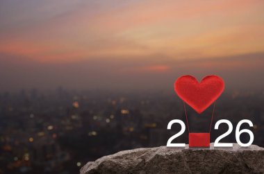 Kırmızı Kumaş Kalp, 2026 beyaz yazılı balonu seviyor. Sıcak gün batımında Rock Dağları 'nda. Mutlu yıllar ve Sevgililer Günü 2026 konsepti.