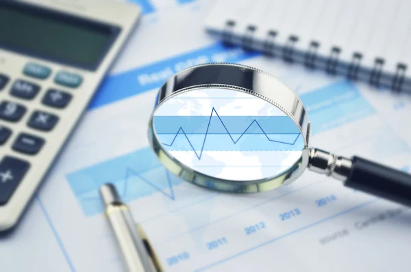 Magnifying glass, calculator and pen on financial graph — Stock Photo, Image