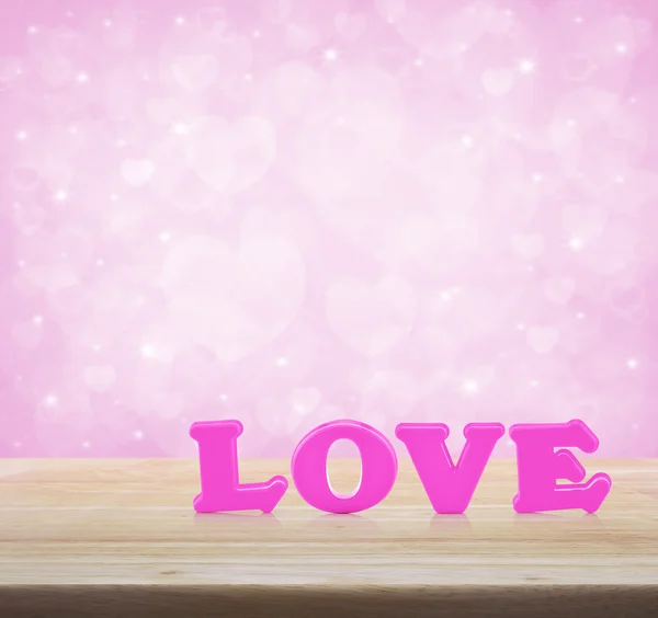 Pink love word on wooden table over light pink heart blur backgr — Stock Photo, Image