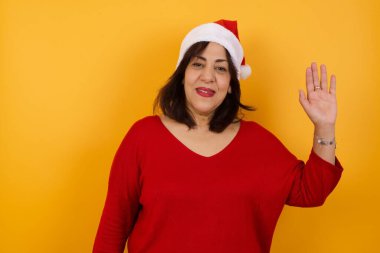 Sarı arka planda duran orta yaşlı Arap kadın selam veriyor ya da elveda diyor mutlu ve güler yüzlü, dostça bir hoş geldin jesti