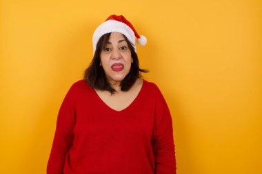 Mutlu ve komik yüzlü, gülümseyen ve dil gösteren Noel şapkası takan orta yaşlı güzel bir Arap kadın..